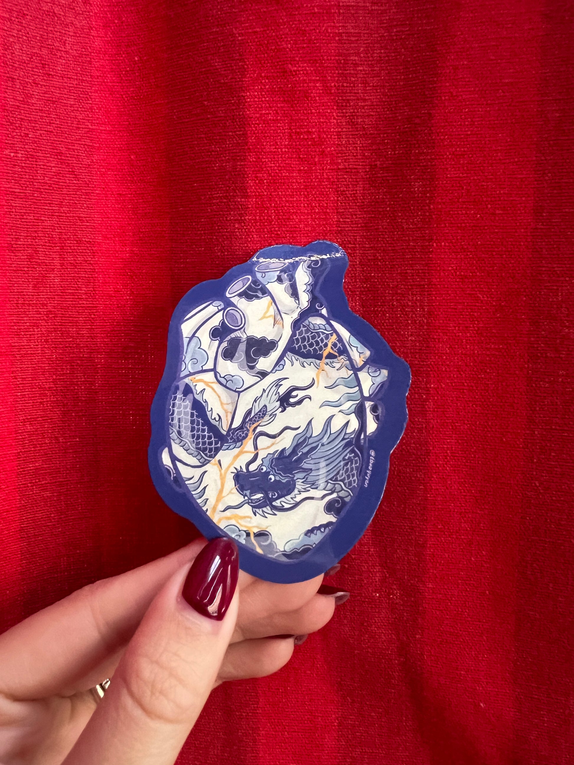 Hand holding a blue and white sticker in the shape of a heart against a red background