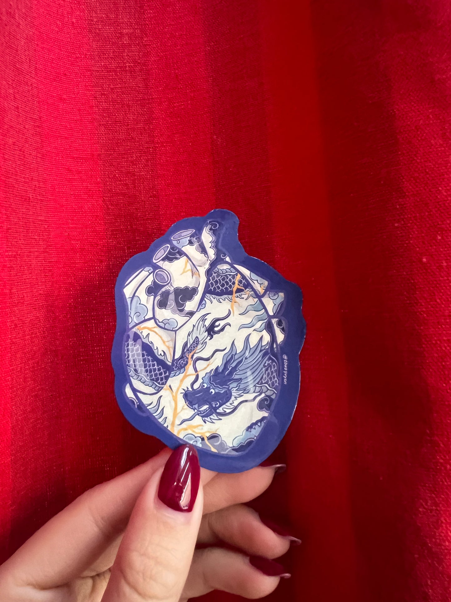 Hand holding a blue and white sticker in the shape of a heart against a red background
